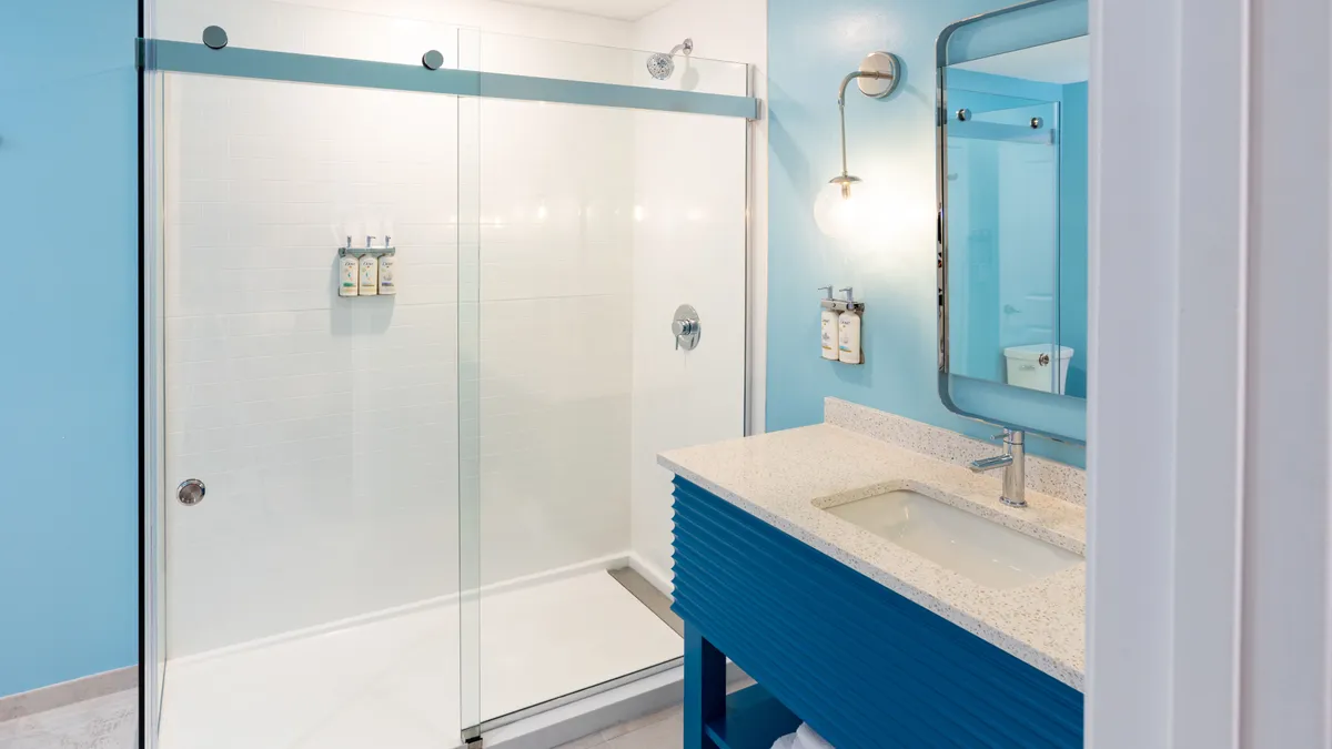 This photo captures the bathroom’s modern walk-in glass shower, a sleek blue vanity, and a well-lit mirror. The finishes and fixtures are clearly upgraded, emphasizing the space’s calming, spa-like quality ideal for unwinding and self-care routines.